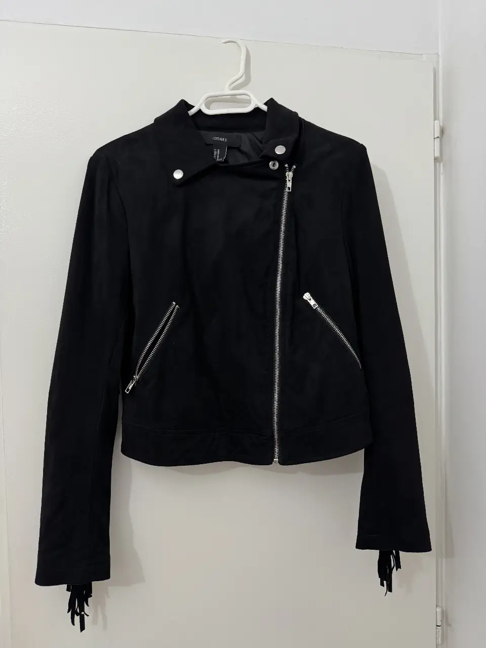 Campera biker de gamuza sintética negra, con cierre y bolsillos con cremalleras. Detalles de flecos en las mangas. Ideal para un look rockero y canchero.