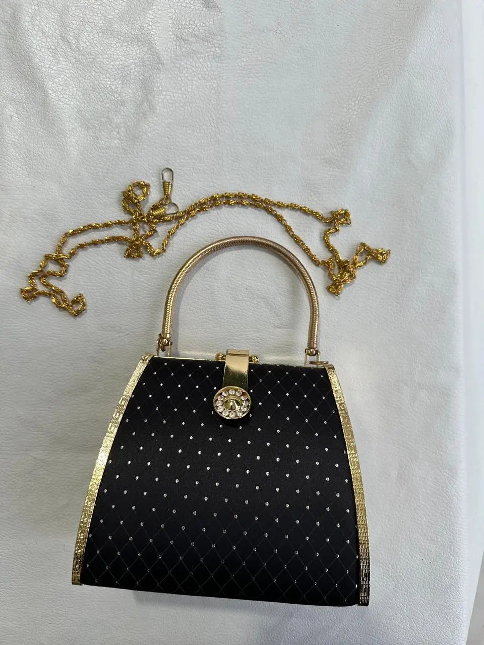 Cartera de mano negra con detalles dorados y cadena dorada. Ideal para eventos formales y fiestas.