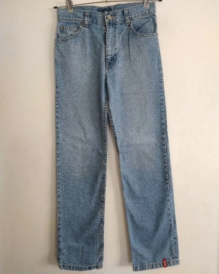 Jean de algodón celeste con detalles de parches en los bolsillos traseros. Uno de los parches tiene el número "95" en rojo y el otro es un logo de la marca OshKosh B'gosh. El parche de atrás está sobre un enganche d jean.