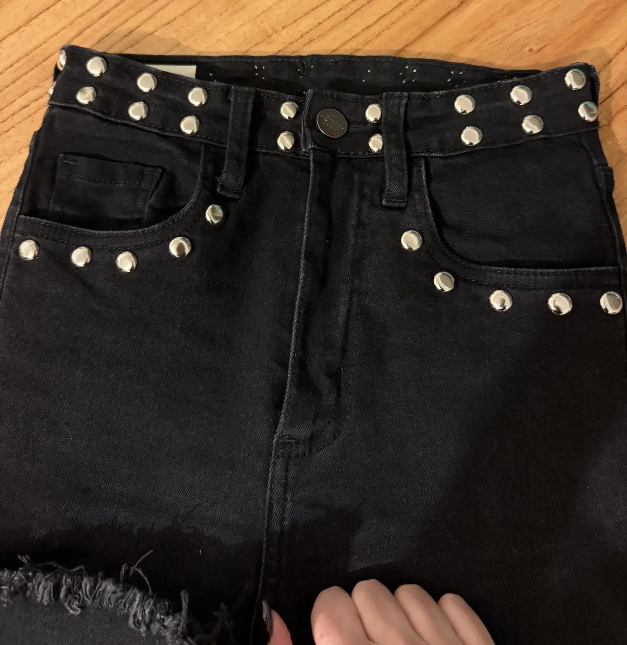 Jean negro elastizado XS/S con tachas plateadas y puntas flare semi desflecadas marca Chic Denim. Tiro medio, con detalles de tachas en los bolsillos y cintura. Ideal para un look rocker y canchero.