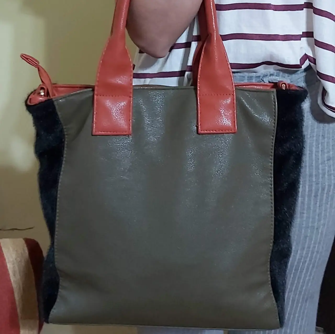 Cartera de mano con detalles en piel sintética de color verde y naranja. Posee detalles de peluche negro en los laterales. Ideal para un look casual y moderno. Trae correa para uso como morral. Poco uso.