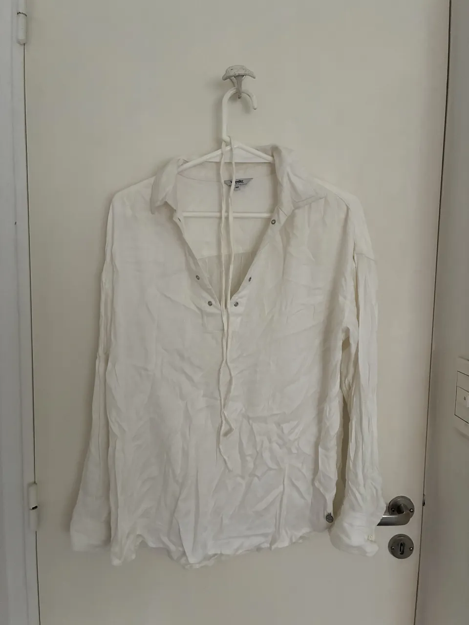 Camisa blanca de manga larga, con cuello y cordones para ajustar en el escote. Perfecta para un look casual y fresco.