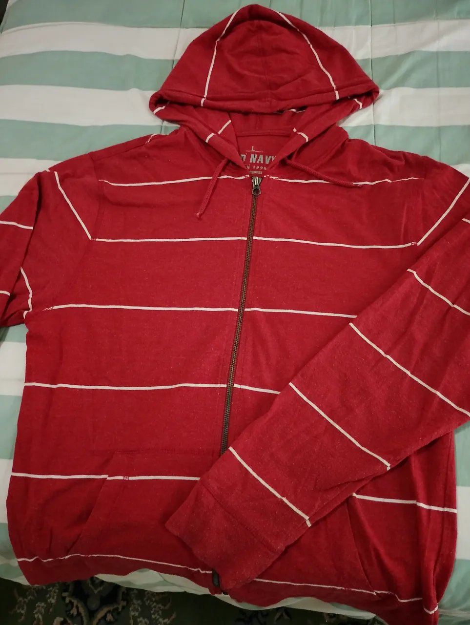 Buzo con capucha y cierre completo, de color rojo con rayas blancas horizontales. Ideal para un look casual y cómodo.