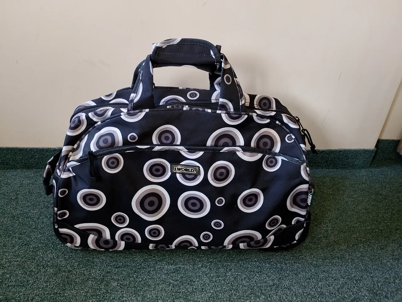 Bolsa de viaje J World con diseño de círculos en blanco, negro y gris. Ideal para escapadas de fin de semana o para llevar tus pertenencias a la playa o a la montaña. Cuenta con ruedas y manija extensible para facilitar su transporte.