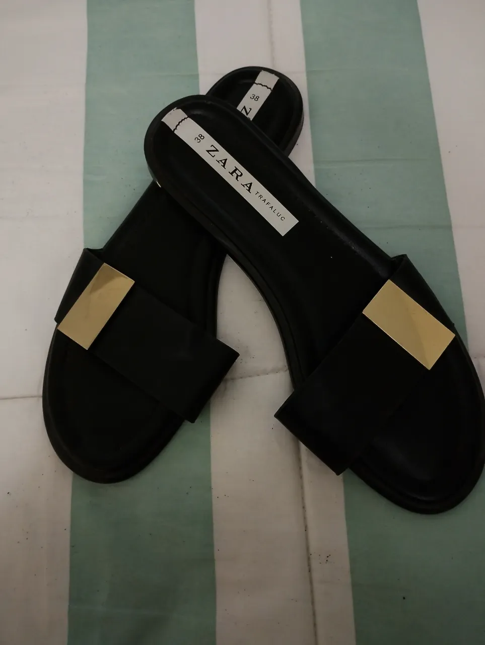 Sandalias negras de tiras con detalle metálico dorado. Perfectas para un look casual y moderno.