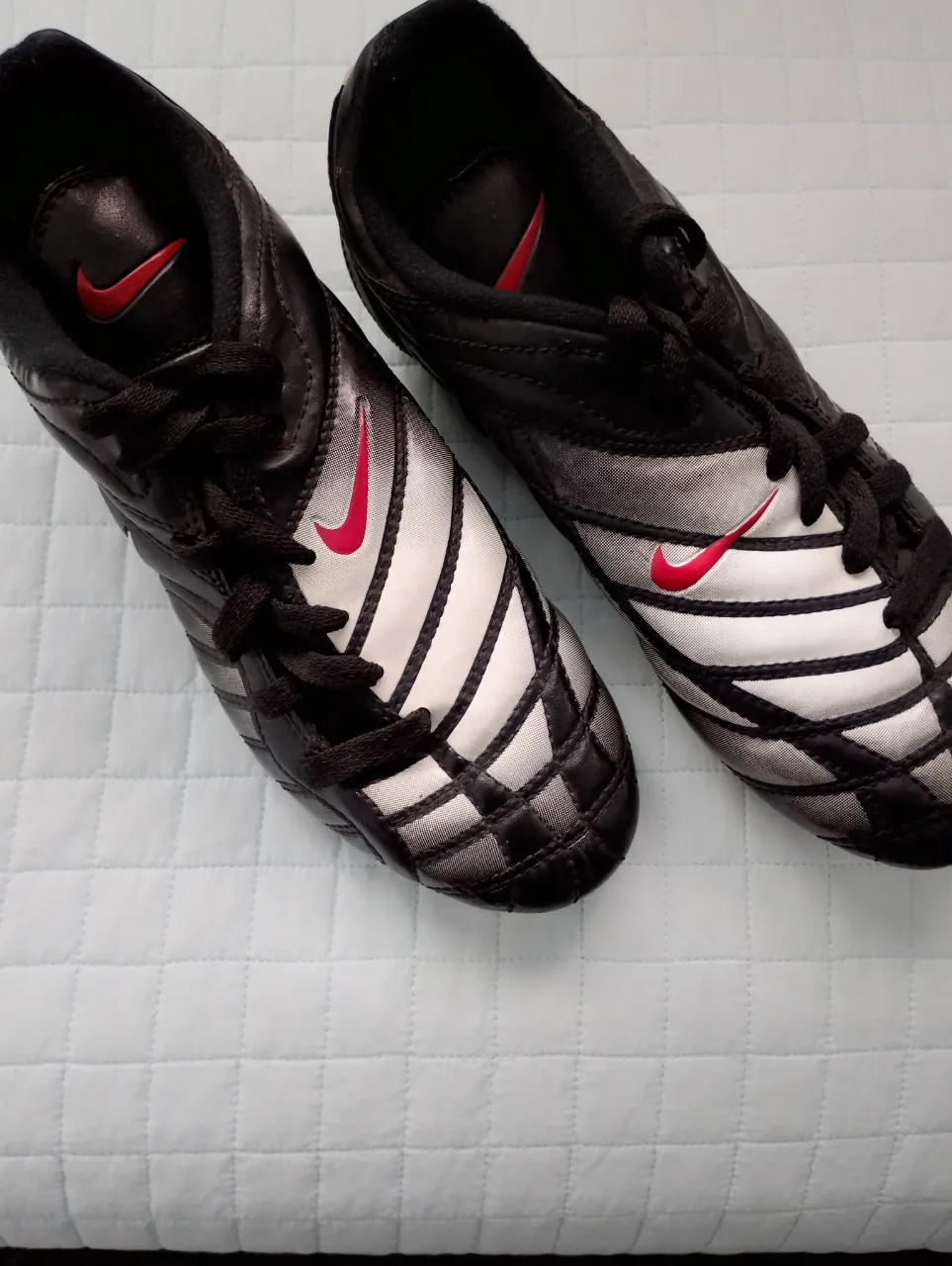 Botines de fútbol Nike para niños, ideales para entrenar y jugar en la cancha. Diseño moderno en negro y plateado con detalles en rojo. ¡Listos para la acción!