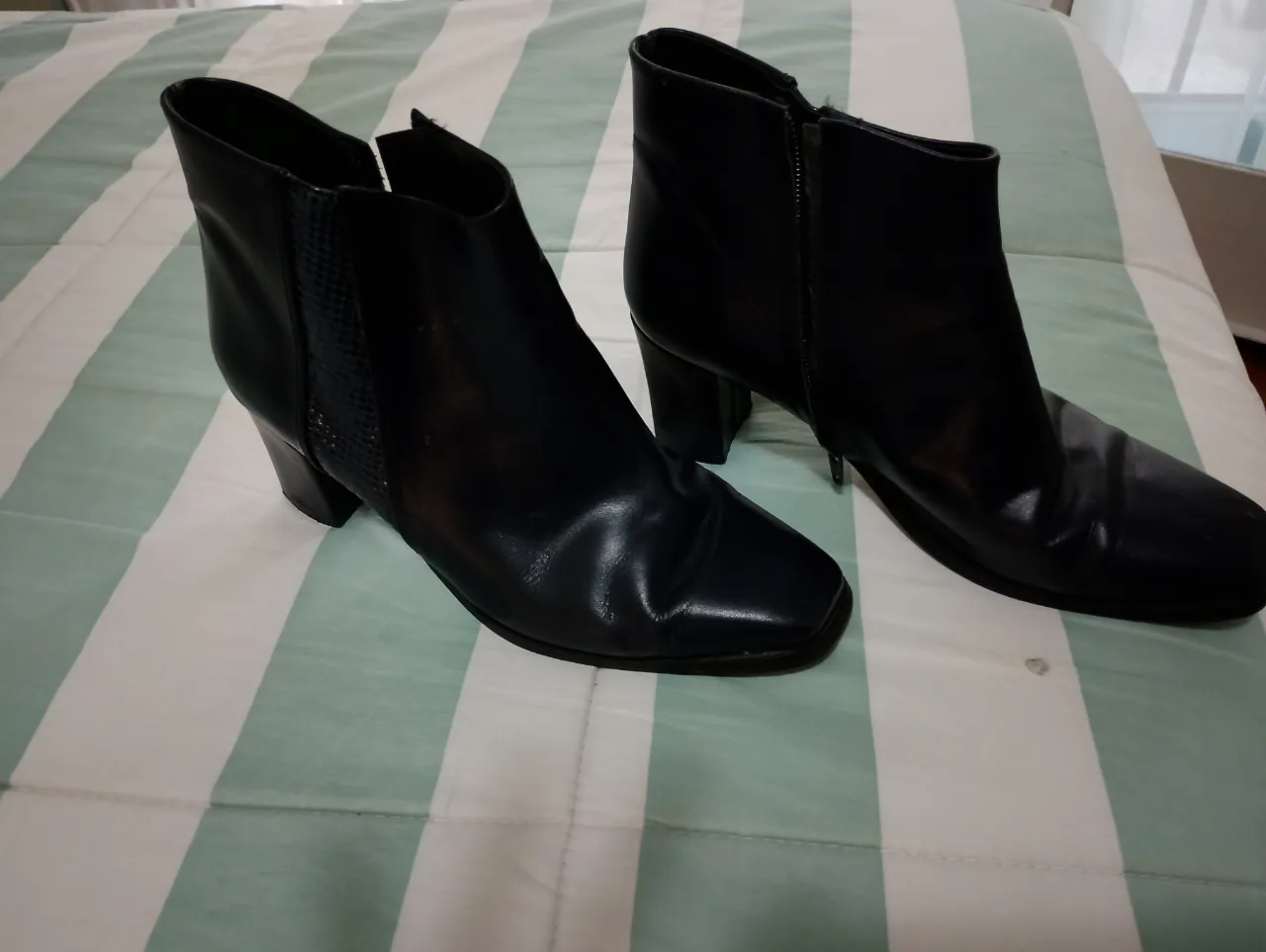 Botitas negras de cuero con taco. Tienen cierre lateral y un detalle de textura tipo reptil en los laterales. Ideales para un look canchero y elegante.