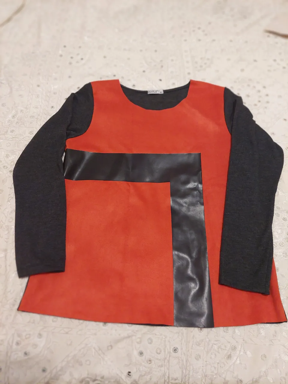 Remera manga larga con detalles en cuero sintético y gamuza. Diseño moderno y original, ideal para un look canchero y urbano. El frente es naranja y negro, las mangas y la espalda son gris oscuro.