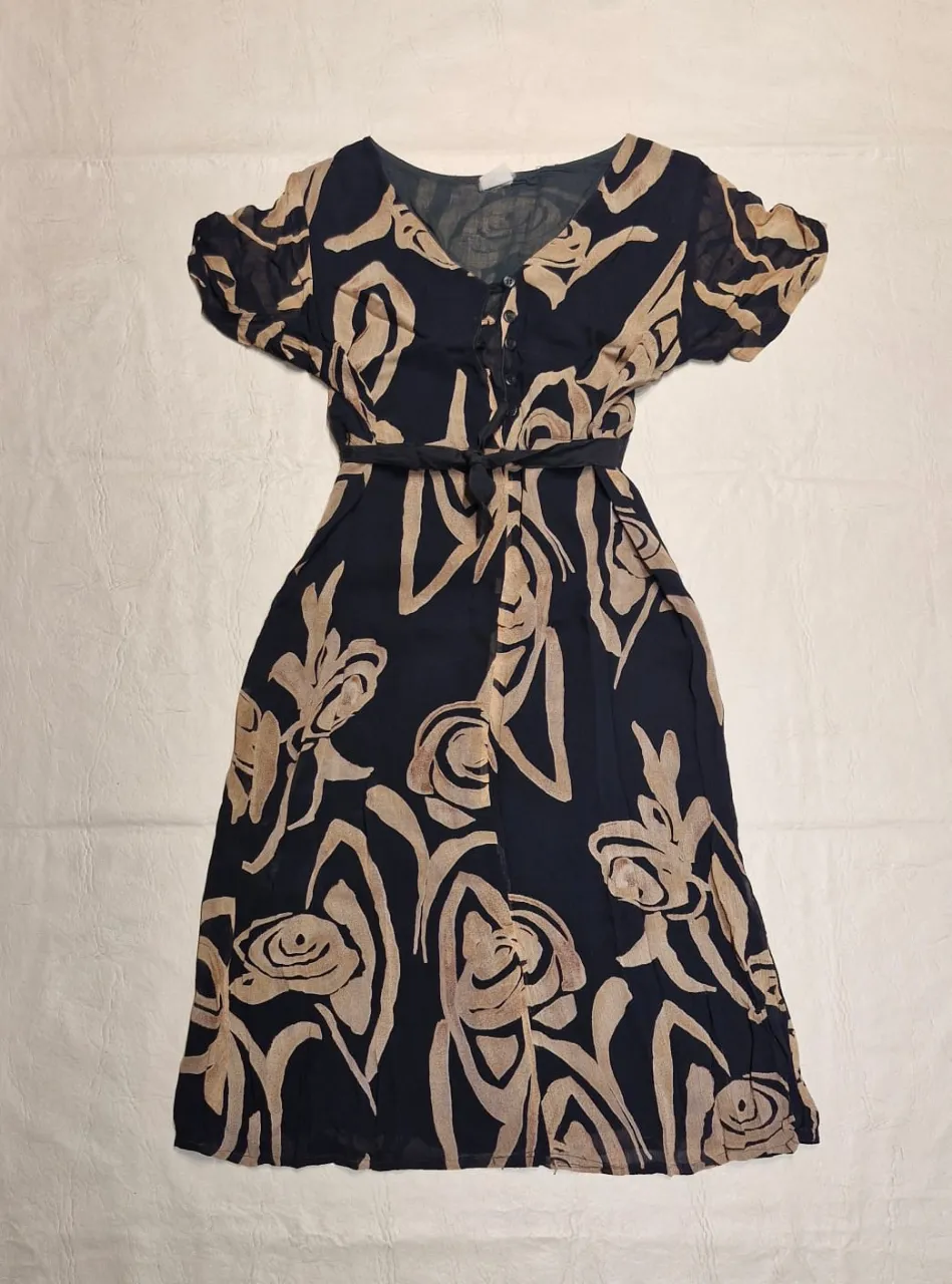 Vestido midi con estampado floral abstracto en tonos negro y beige. Corte en la cintura con cinturón, mangas cortas y escote en V con botones. Ideal para un look casual y fresco.