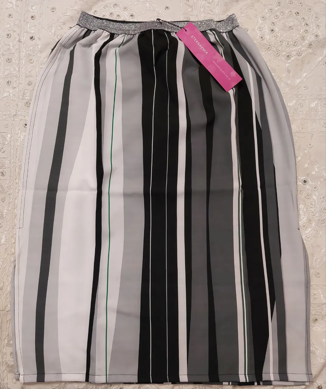 Pollera midi con estampado de rayas verticales en tonos negros,  grises y blanco con pequeñas líneas verdes. Posee cintura elastizada con detalle plateado y tajo a los costados. Medidas:
Largo: 70 cm
Contorno de cintura 62 cm.
Contorno de cadera 116 cm.