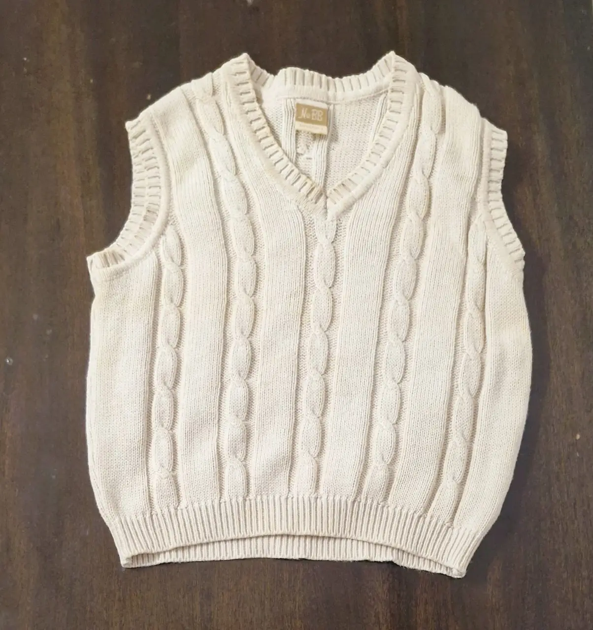 Chaleco tejido de punto de hilo para niño, color crudo, con diseño de trenzas. Cuello en V y etiqueta de la marca NuBB.