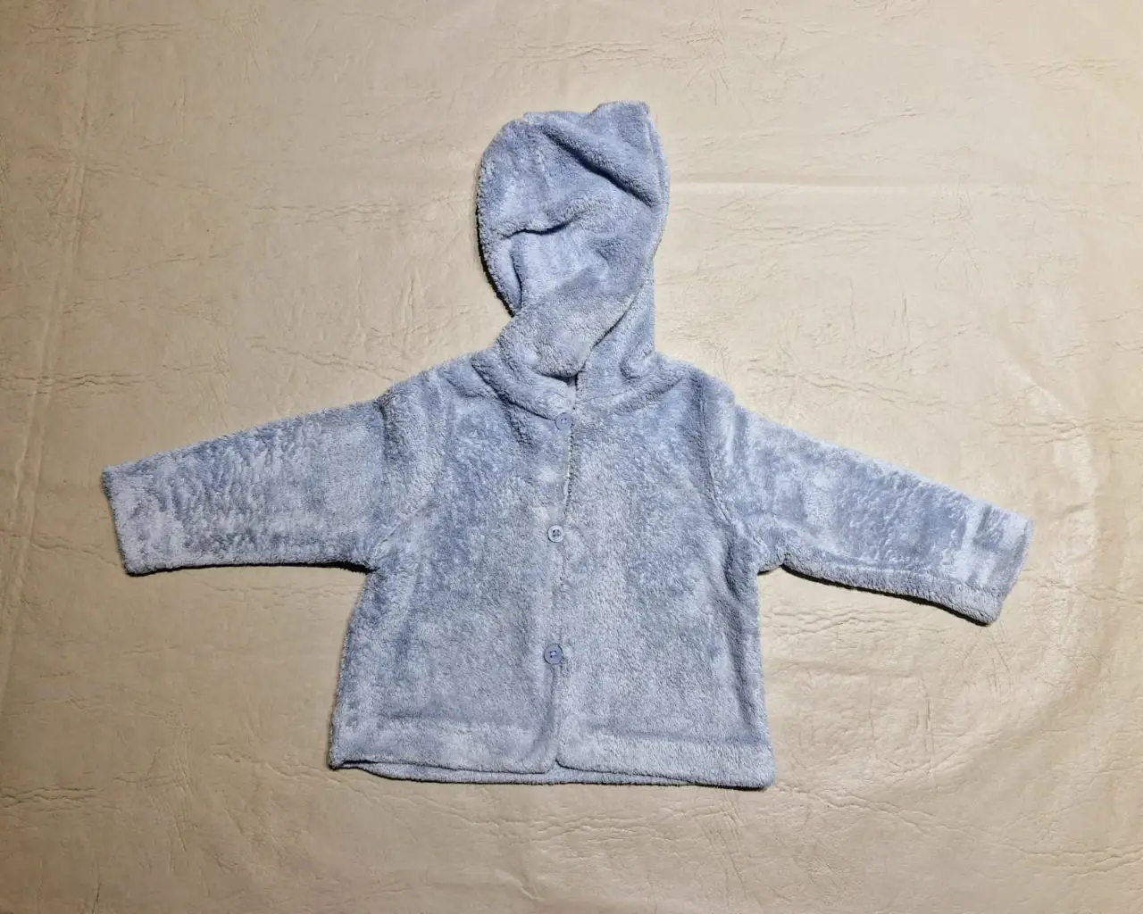 Buzo de bebé con capucha, de tela suave y abrigada, ideal para el invierno. Exterior de plush, interior de algodón. Cuenta con botones al frente para facilitar su colocación y un diseño cómodo para el día a día.