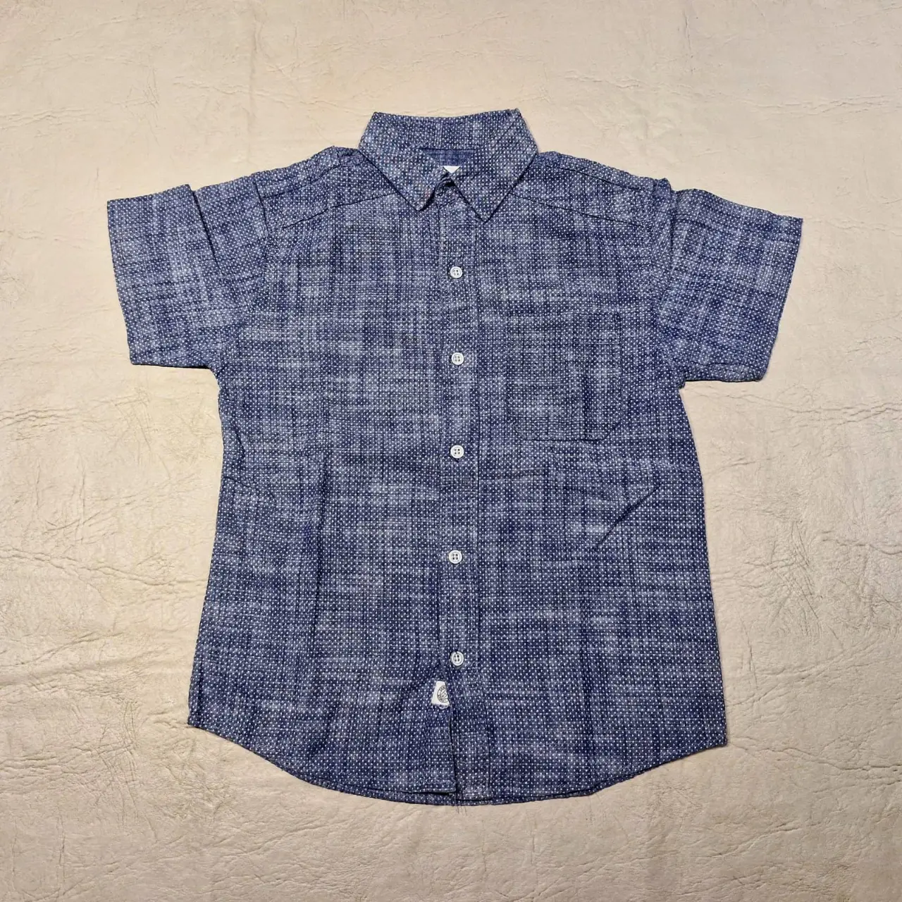Camisa de niño celeste. Tela tramada en azul y blanco. Manga corta, con bolsillo en el pecho y cuello clásico. Ideal para un look casual y fresco.