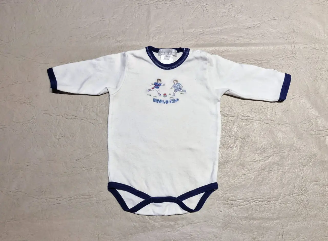 Body de bebé blanco con detalles en azul marino. Estampado de dos niños jugando al fútbol con la leyenda "WORLD CUP". Ideal para los más pequeños.