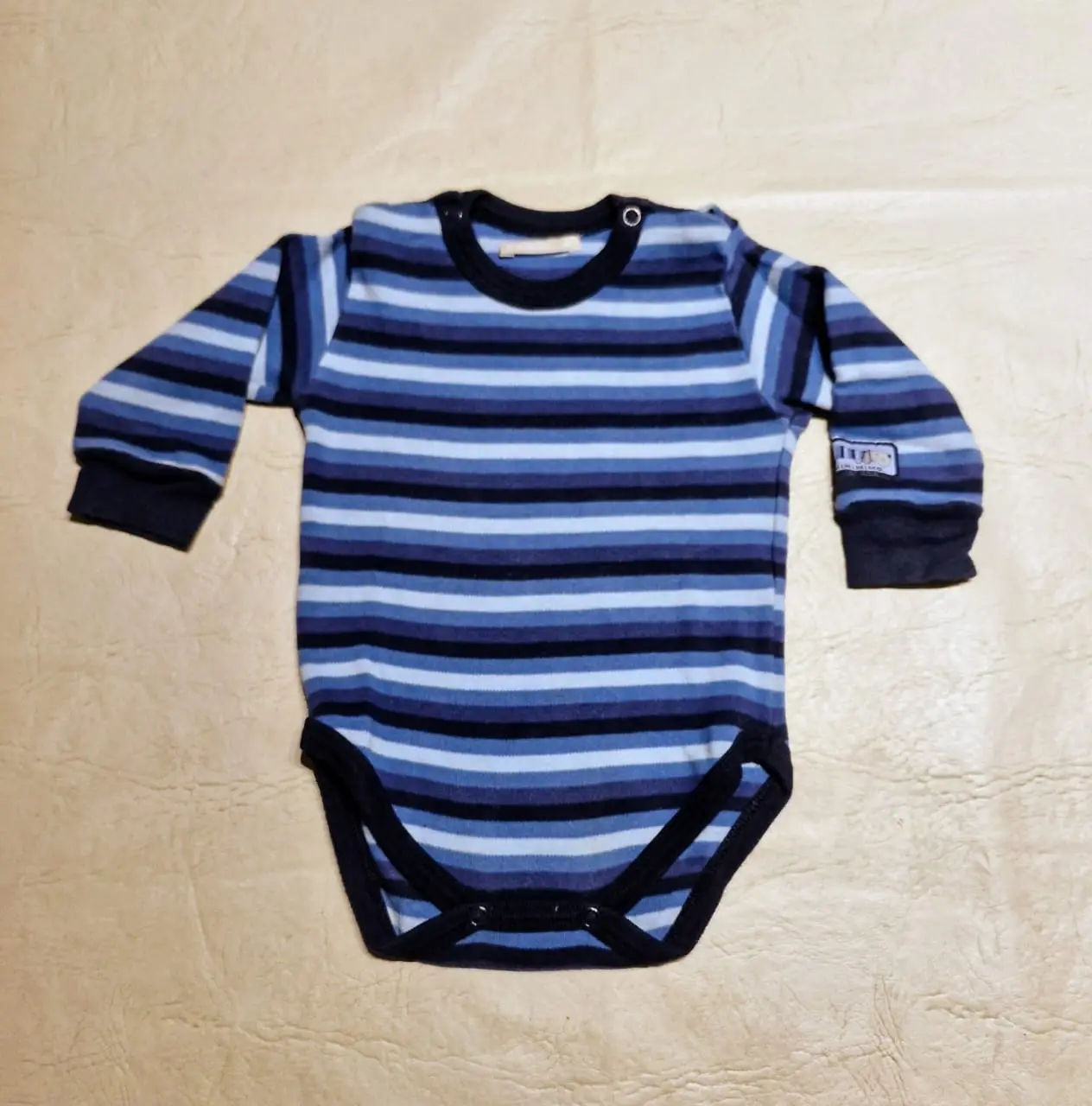 Body de bebé a rayas horizontales en tonos azules y celestes, con mangas largas y cuello redondo. Ideal para mantener a tu bebé cómodo y abrigado.
