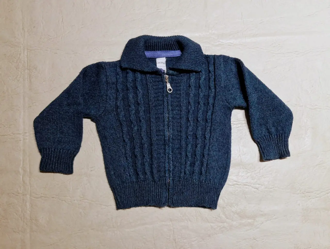 Sweater de niño azul con cierre frontal y cuello tipo chomba. Diseño tejido con detalles en relieve. Ideal para el invierno.