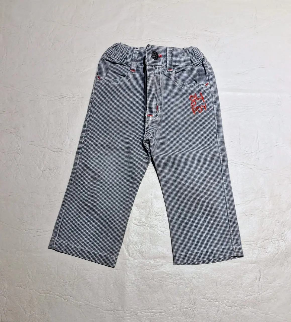 Pantalón de niño, modelo tipo jean, a cuadros celeste oscuro y blancos, con detalles en rojo. Tiene cintura elastizada, con elástico interno para regular y cierre con botón y cremallera. Ideal para un look casual y cómodo.