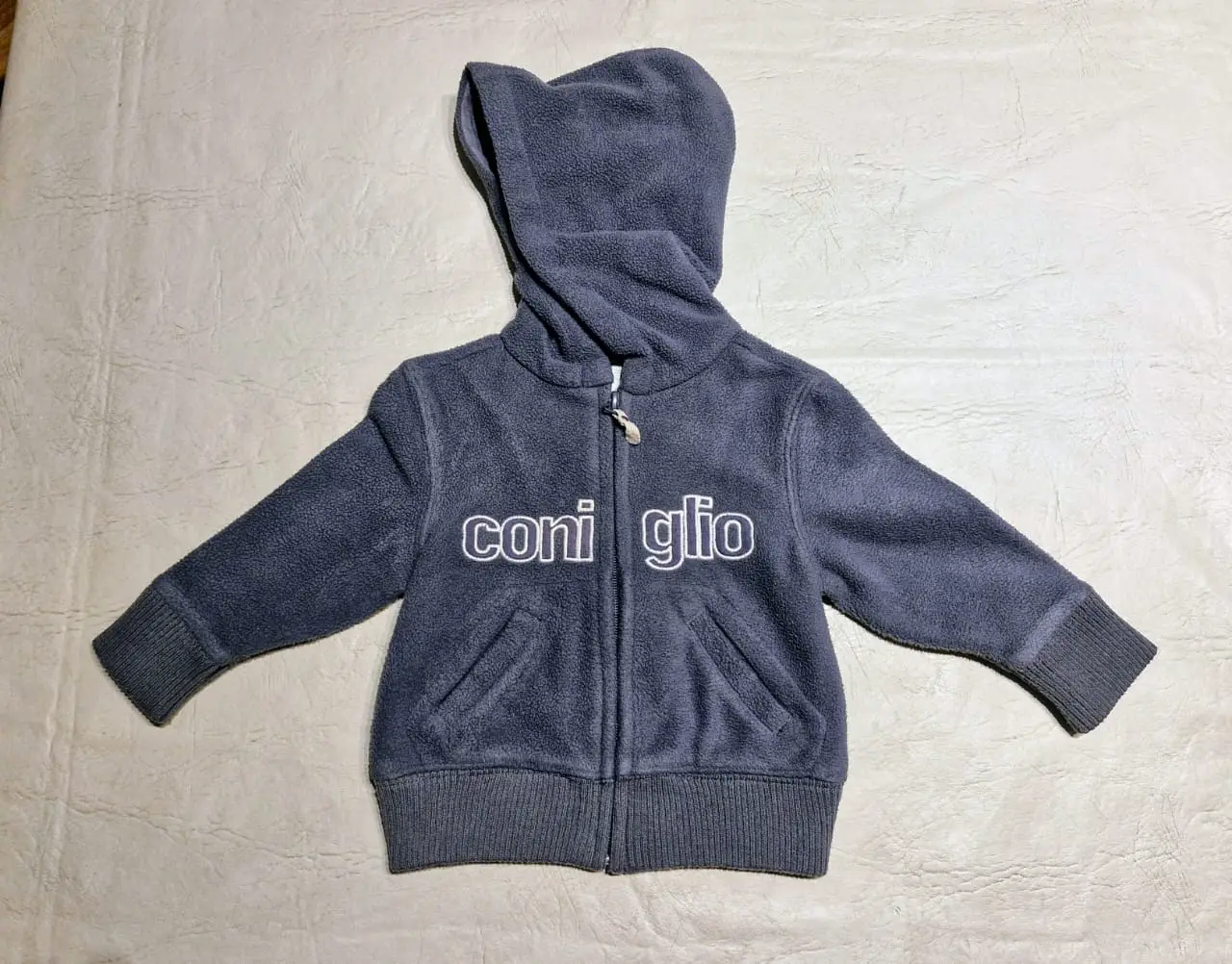 Buzo con cierre para niño, de polar color gris, con capucha y la marca "Coniglio" estampado en blanco. Ideal para el invierno.