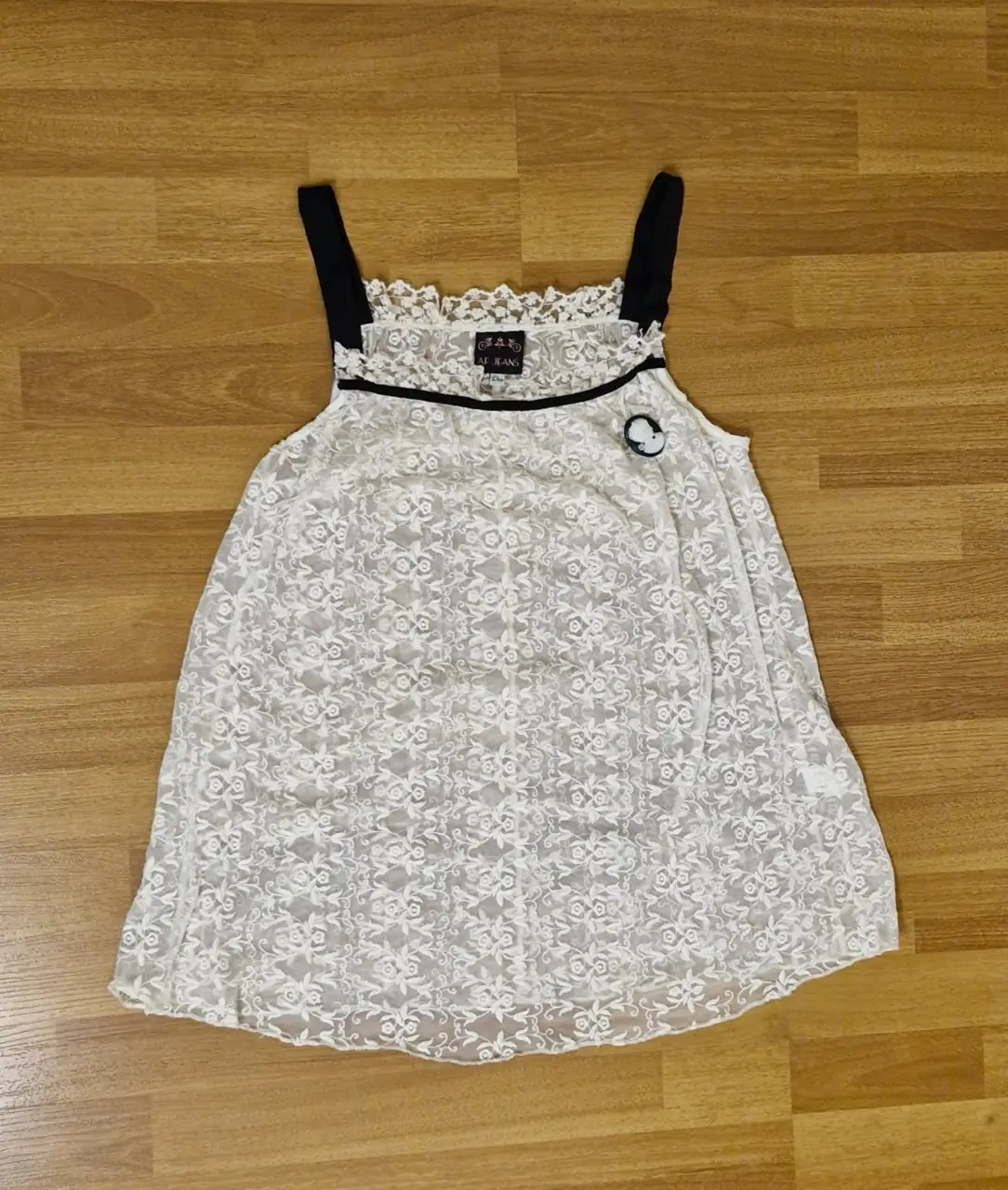 Blusa de encaje blanca con detalles y breteles en negro. Con un prendedor que se puede retirar. Ideal para un look romántico y delicado.