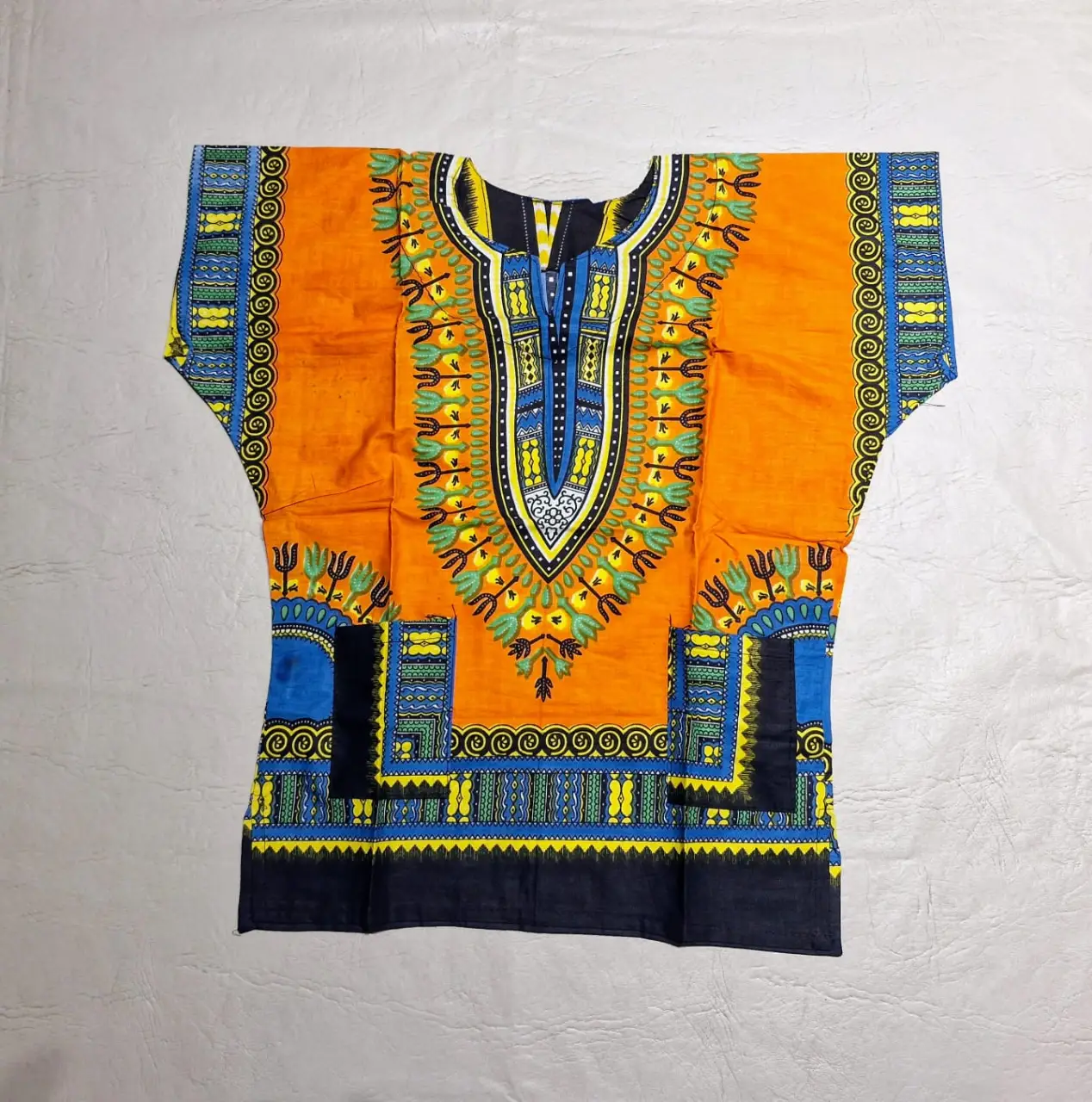 Camisa Dashiki africana para niños con estampado vibrante en naranja, azul y negro. Diseño tradicional con cuello en V y detalles geométricos, con dos bolsillos en el frente. Ideal para un look étnico y con estilo o para disfraz.