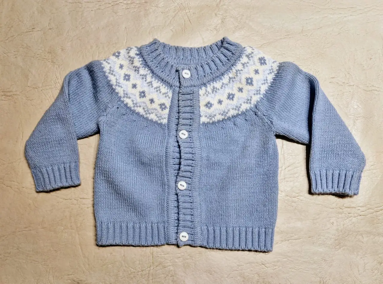 Cárdigan de bebé de lana celeste con diseño en blanco en el canesú. Artesanal realizado en Salta. Ideal para mantener a tu bebé abrigado con estilo y comodidad.