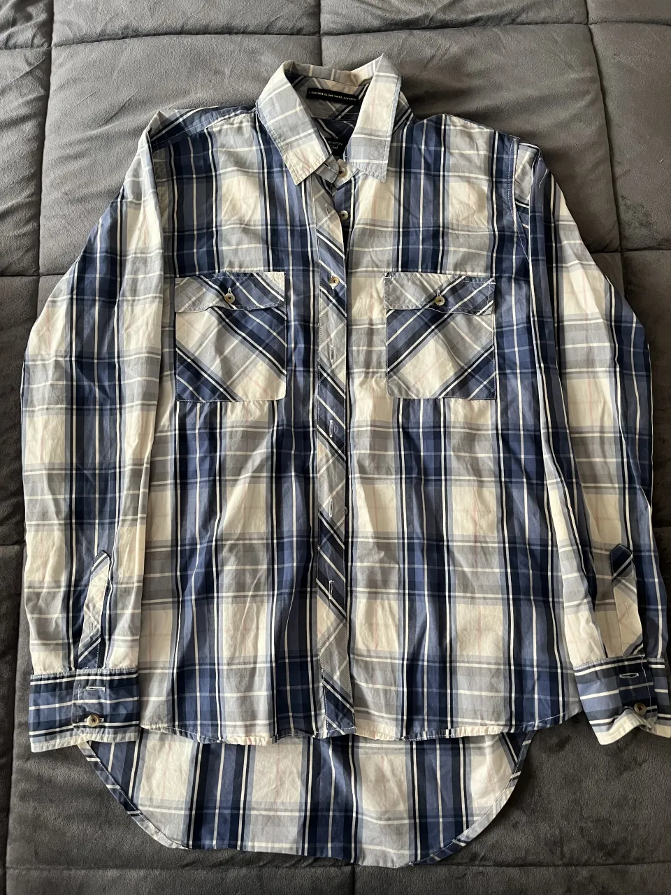 Camisa de leñador kevingston, a cuadros en tonos azules y blancos. Posee dos bolsillos en el frente y botones.