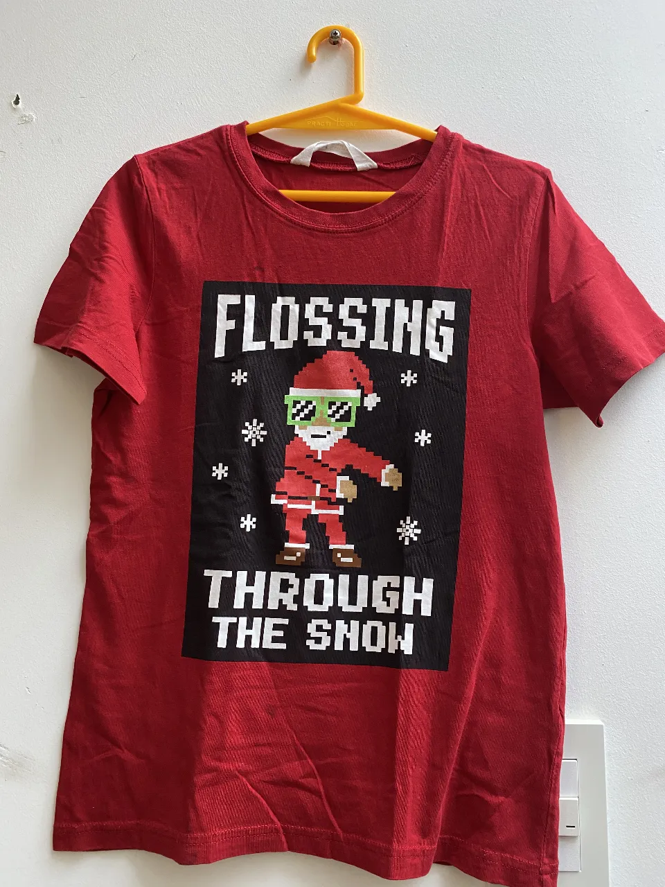 Remera roja de algodón con estampado navideño. Diseño divertido con un Santa Claus pixelado haciendo el "floss". Ideal para celebrar las fiestas con estilo. Tiene una manchita que se ve en la foto