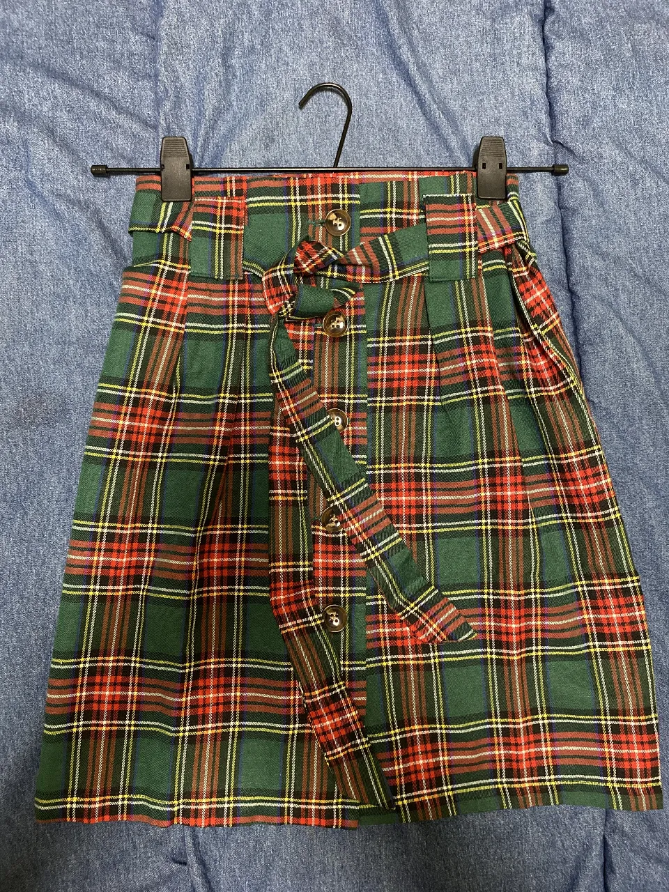 Pollera escocesa con diseño a cuadros en tonos verdes, rojos y amarillos. Cuenta con un cinturón a juego y botones decorativos. Ideal para un look vintage y preppy. Talle S
