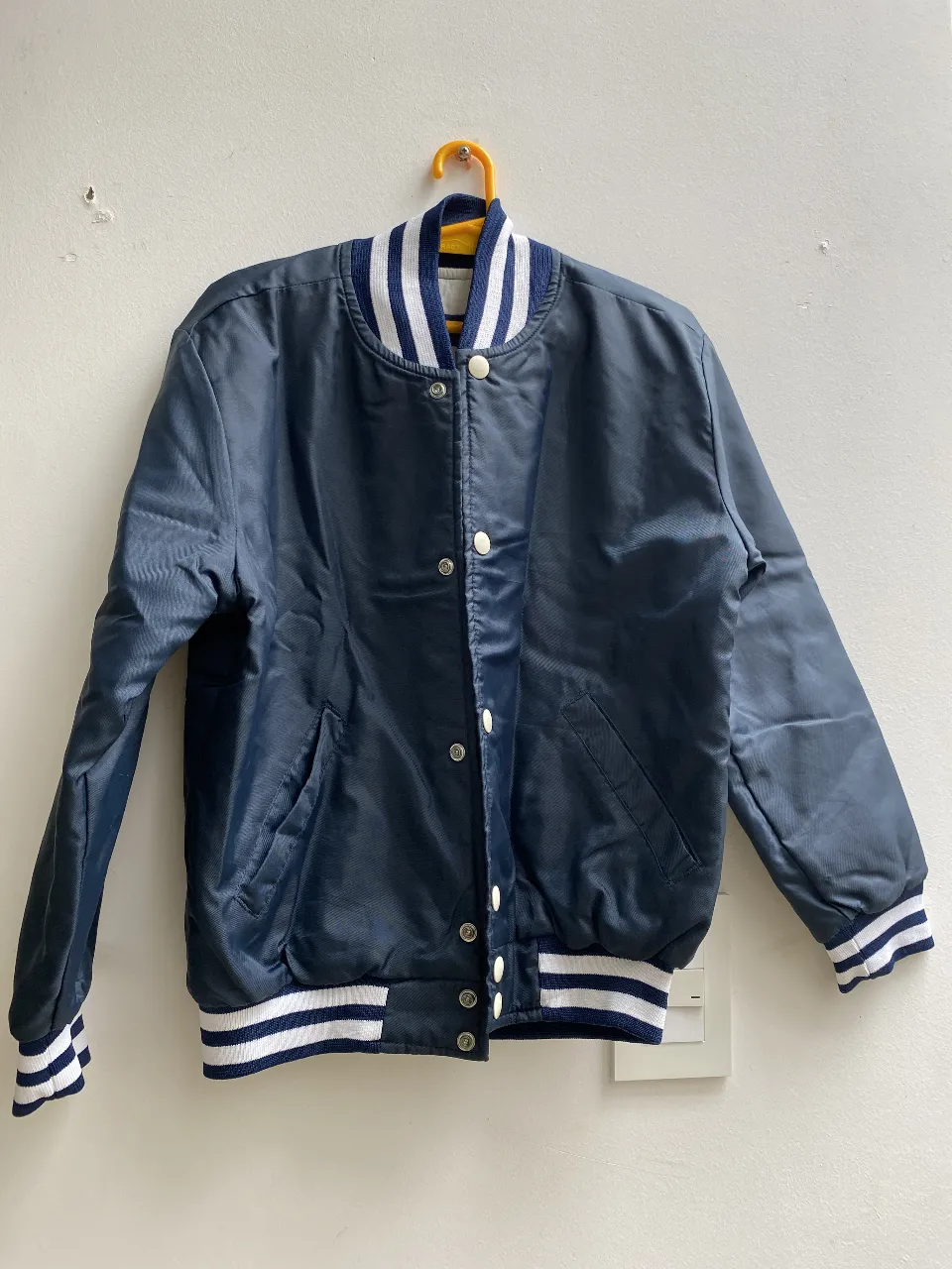 Campera bomber azul marino con detalles en blanco. Cuello, puños y cintura con rayas blancas. Cierre frontal con botones. Ideal para un look casual y deportivo. Interior de Matelase. talle 10/12