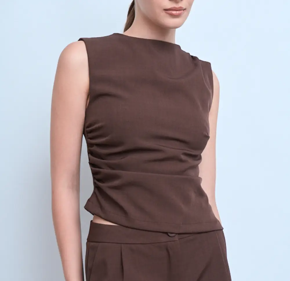 Top sin mangas de diseño moderno, con fruncido lateral que estiliza la figura. Ideal para un look sofisticado y versátil. Talles S o M. Negro Gris Chocolate. 