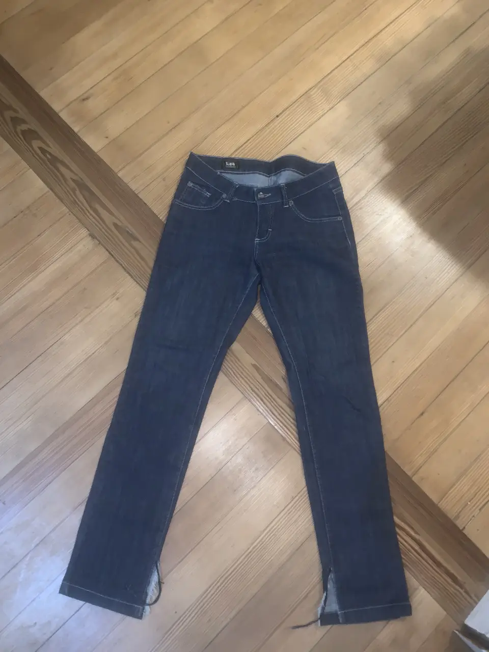 Jeans Lee de mujer, corte recto, color azul oscuro, con detalles de costura en blanco. Posee cierre y botón, y aberturas en los tobillos. Ideal para un look casual y cómodo. 