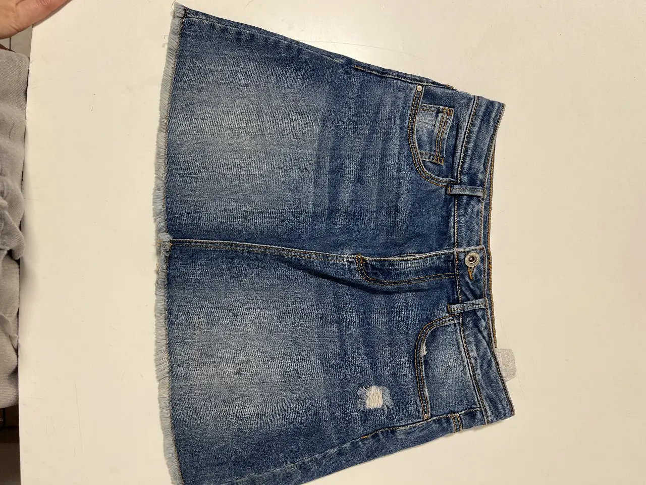 Minifalda de jean azul, con detalles de roturas y flecos en el borde inferior. Ideal para un look casual y moderno.