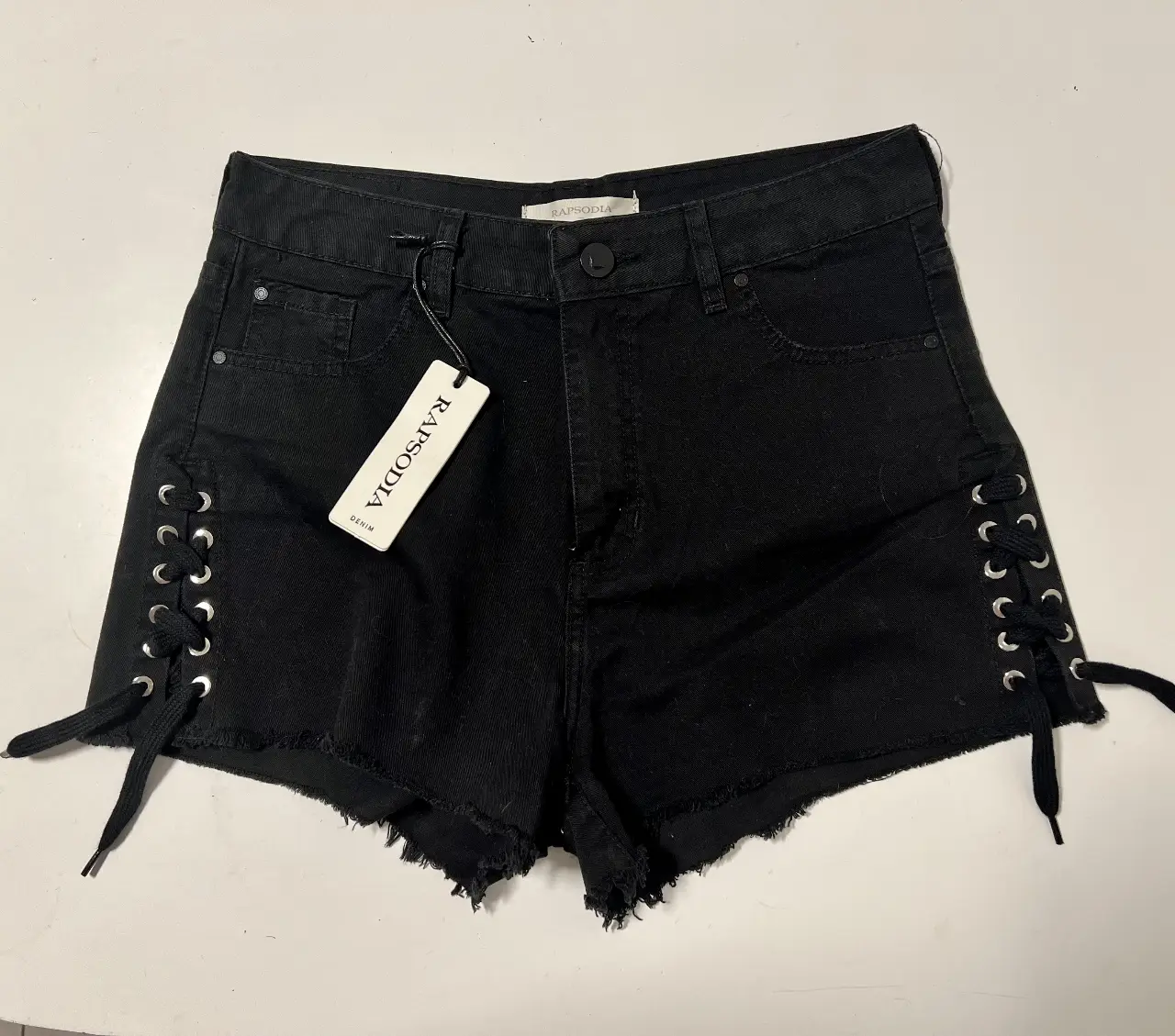 Short de jean negro con detalles de cordones en los laterales y borde desflecado. Ideal para un look casual y moderno. SIN USO. CON ETIQUETA