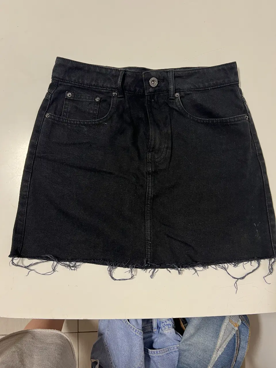 Minifalda de jean negra con detalles desflecados en el borde inferior. Tiro medio, ideal para un look casual y moderno.