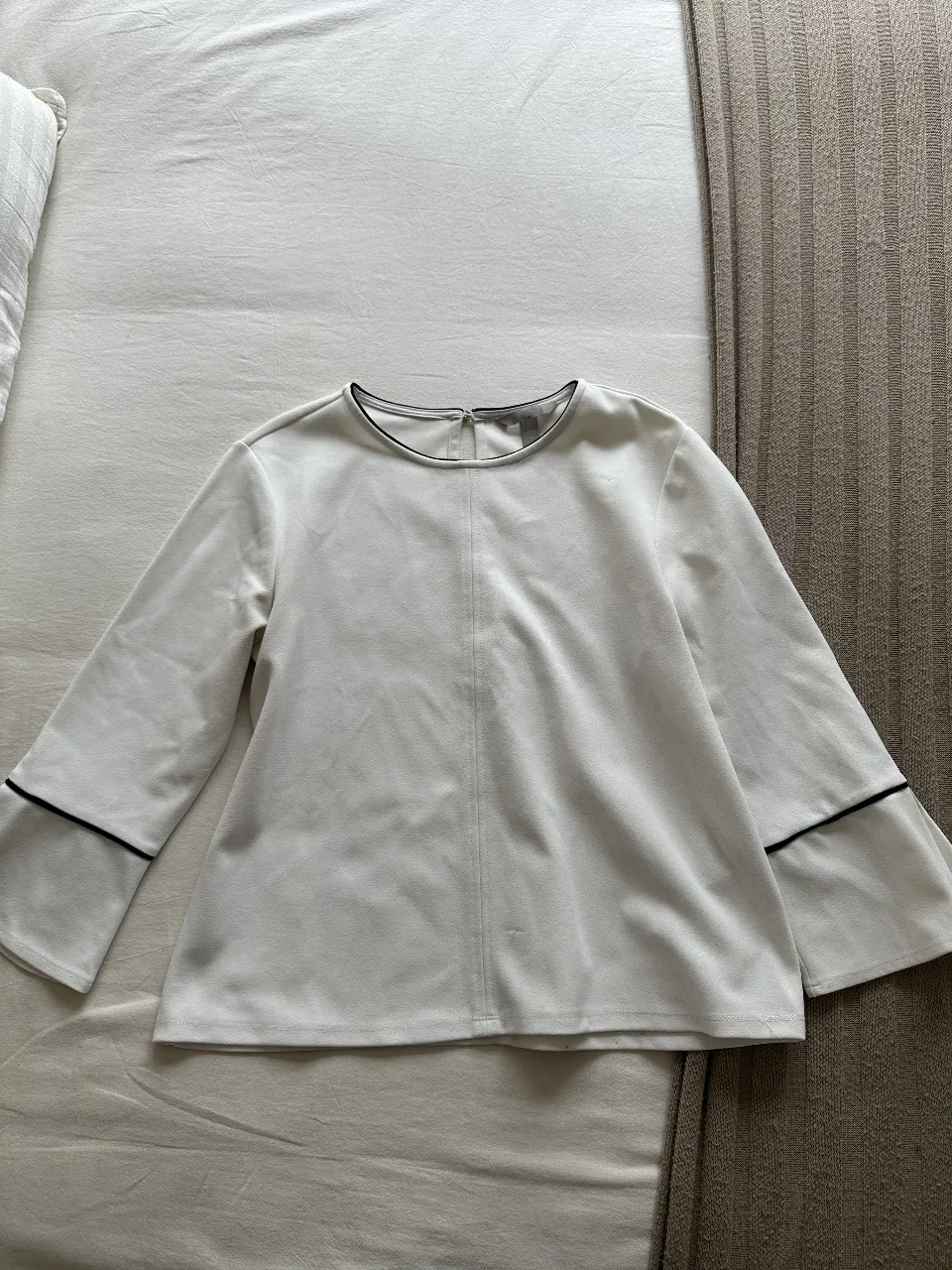 Blusa blanca de manga larga con detalles en negro en los puños y cuello. Ideal para un look elegante y versátil.