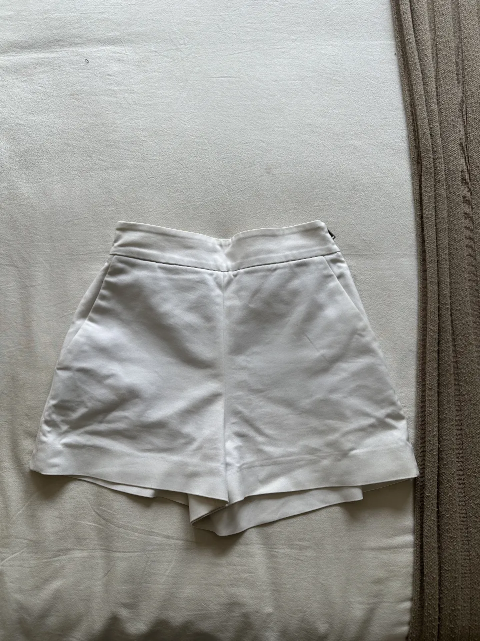 Short sastrero blanco de tiro alto, ideal para un look elegante y moderno. Confeccionado en tela suave y con bolsillos funcionales, perfecto para combinar con blusas o tops.