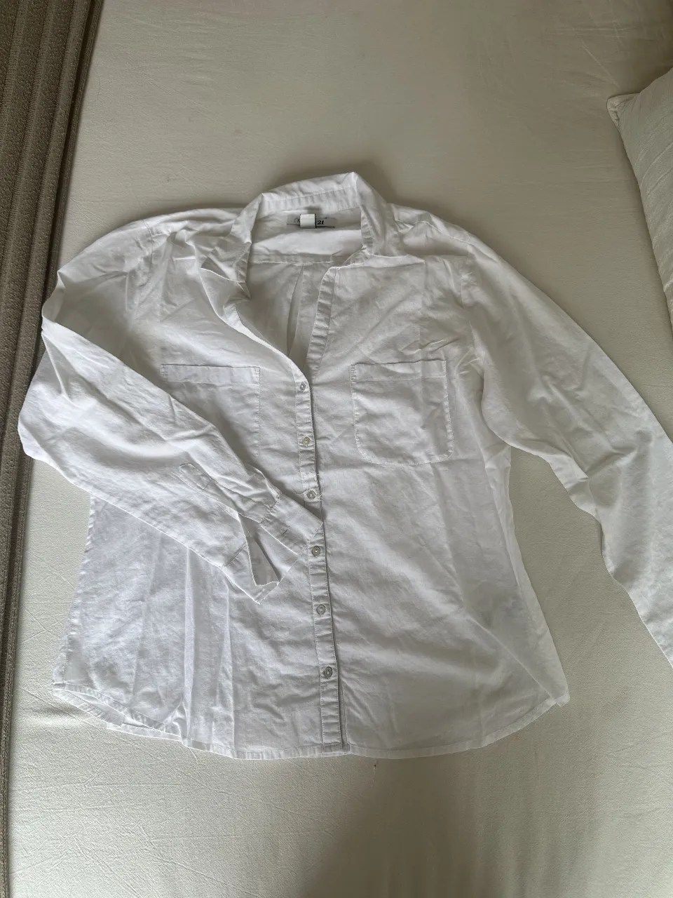 Camisa blanca de mujer, manga larga, con dos bolsillos delanteros. Ideal para un look casual y versátil.