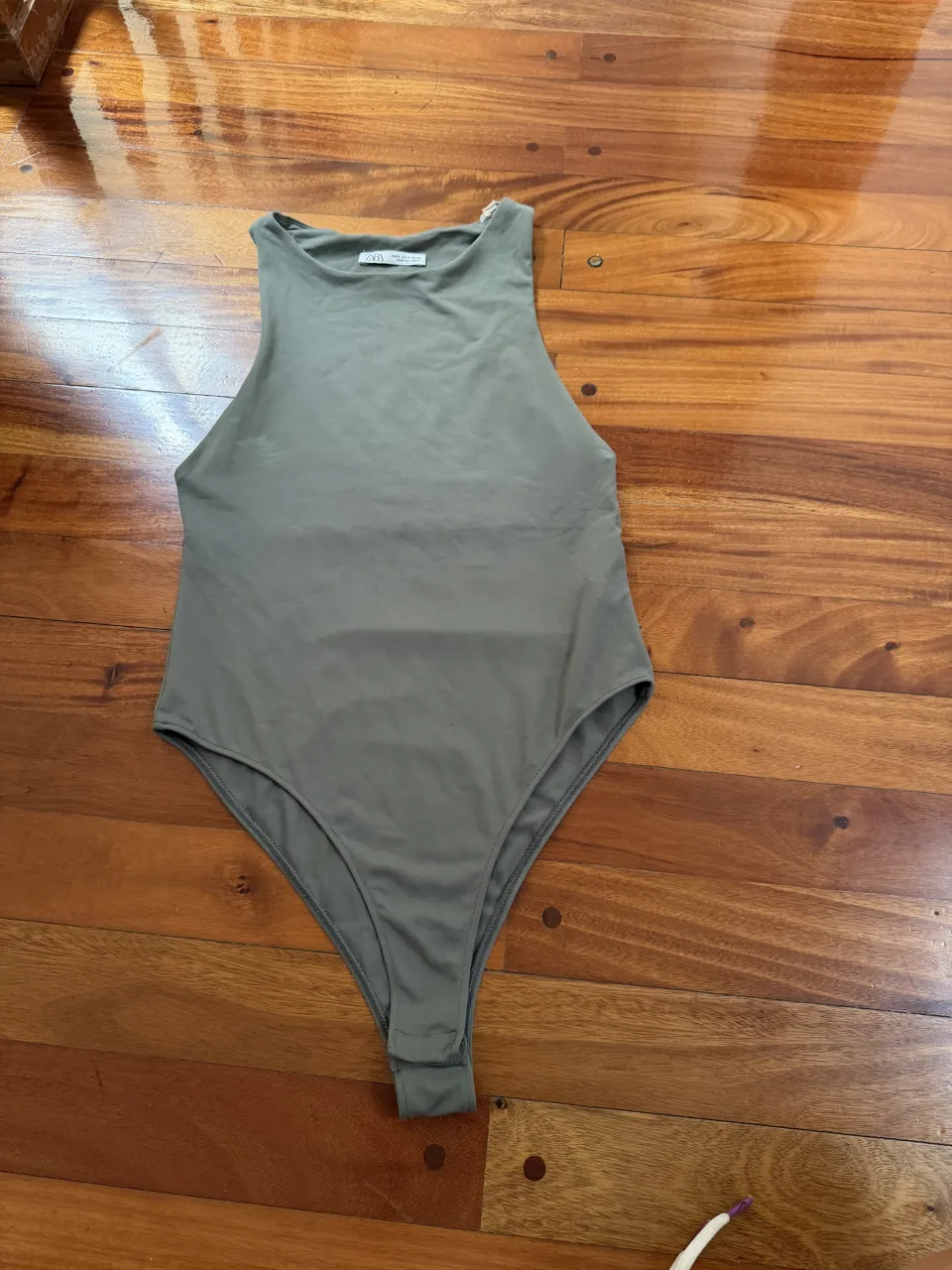 Body de color verde musgo, sin mangas y con cuello redondo. La prenda es de tiro bajo y se abrocha en la parte inferior.