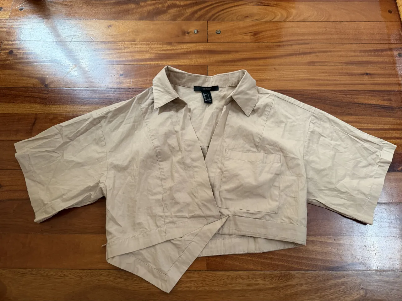 Camisa manga corta color tiza con cuello y solapa. Posee un bolsillo superior izquierdo y un cruce asimétrico en el frente.