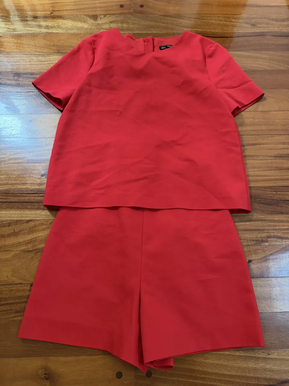 Conjunto de dos piezas rojo, compuesto por una remera de mangas cortas y un short. La remera tiene botones en la espalda.