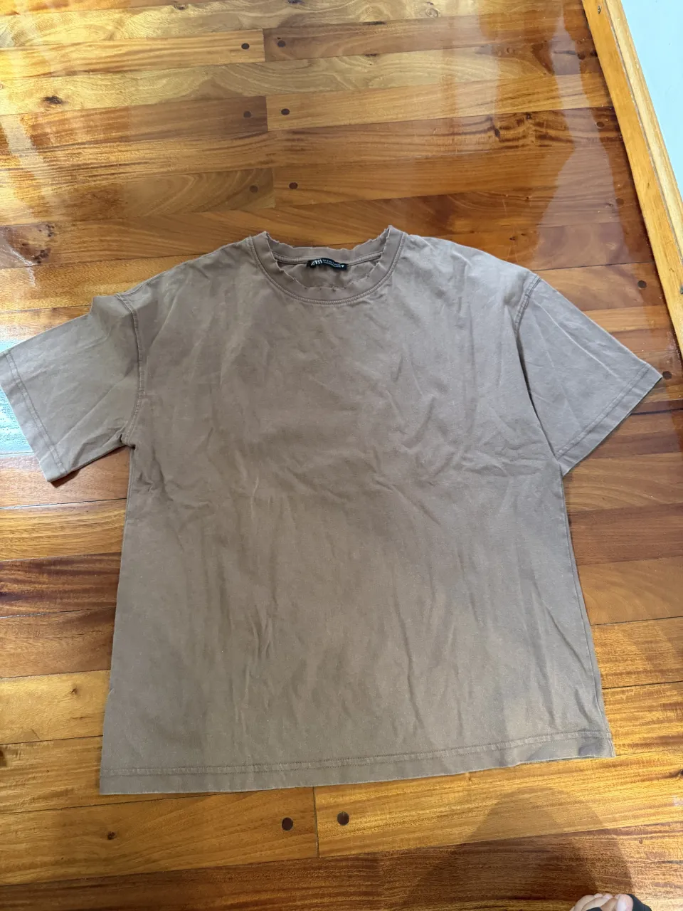 Remera de algodón marrón, con cuello redondo y mangas cortas. Tiene un corte desgastado en el cuello y los bordes, dándole un toque moderno y canchero. Perfecta para el día a día.