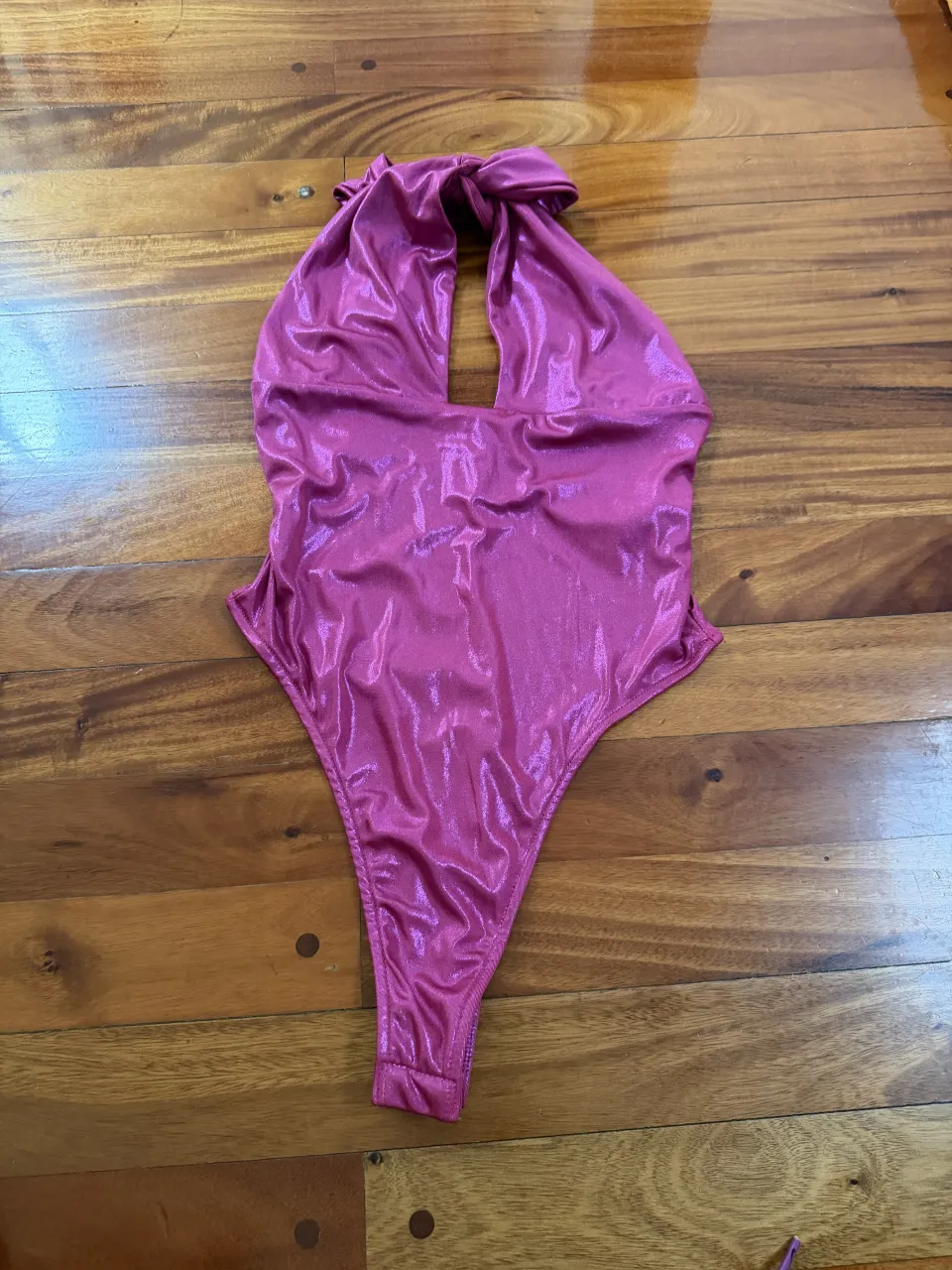 Traje de baño entero color rosa metalizado con cuello halter y lazo en la nuca. Posee un recorte en el escote.