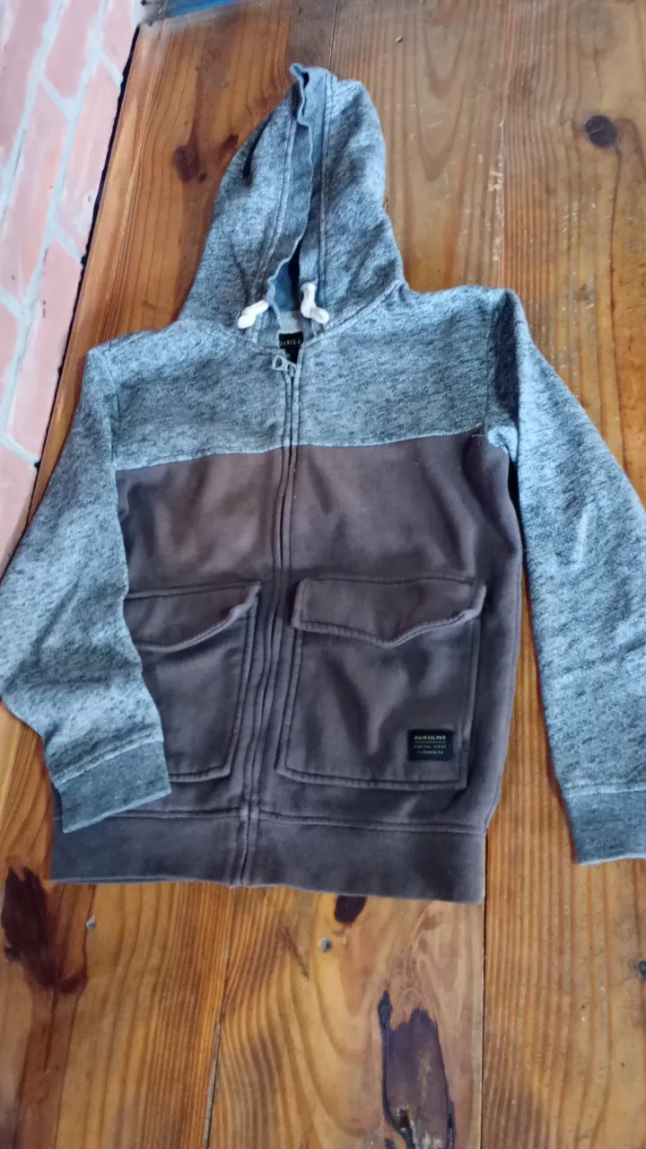 Buzo con capucha y cierre para hombre, de la marca Quiksilver. Confeccionado en una combinación de gris y marrón, este buzo ofrece un estilo casual y cómodo. Cuenta con dos bolsillos frontales y el logo de la marca. Ideal para un look urbano y relajado.