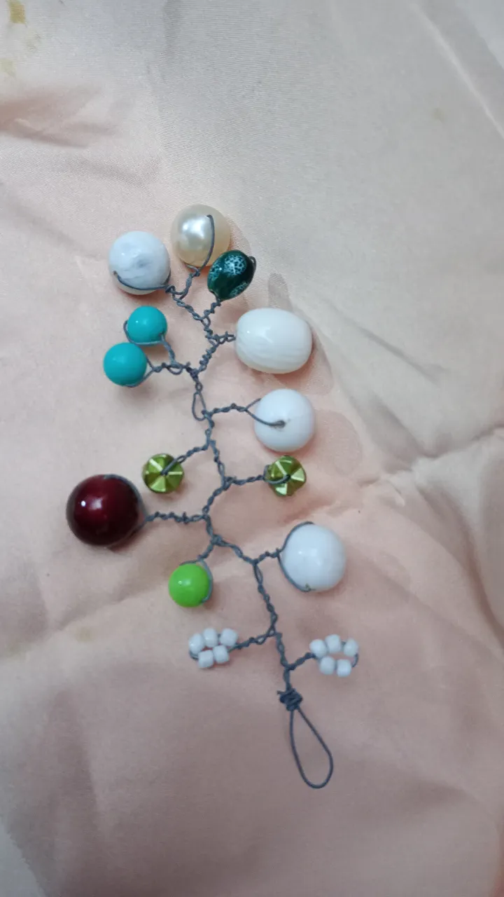 Adorno para el pelo artesanal con diseño de ramas y flores, ideal para eventos especiales o para darle un toque único a tu look diario. Elaborado con alambre y cuentas de diferentes colores y tamaños.