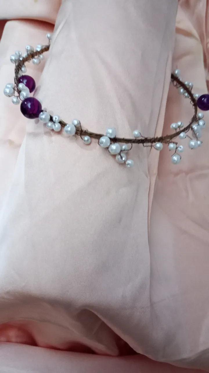 Corona artesanal para el pelo, con base de alambre marrón y adornos de perlas blancas y cuentas violetas. Ideal para eventos especiales o para darle un toque bohemio a tu look.