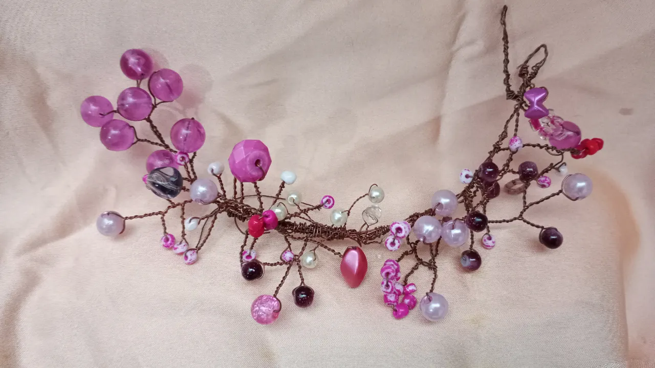 Diadema artesanal con alambre marrón y adornos de cuentas y flores en tonos rosados y violetas. Ideal para eventos especiales o para darle un toque romántico a tu look.
