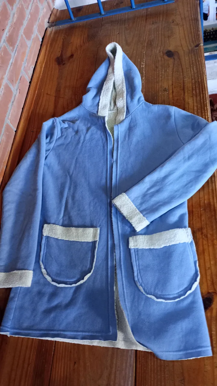 Abrigo de polar azul con capucha y detalles en blanco. Ideal para estar cómoda en casa o estilo casual. Bolsillos amplios interior de corderito