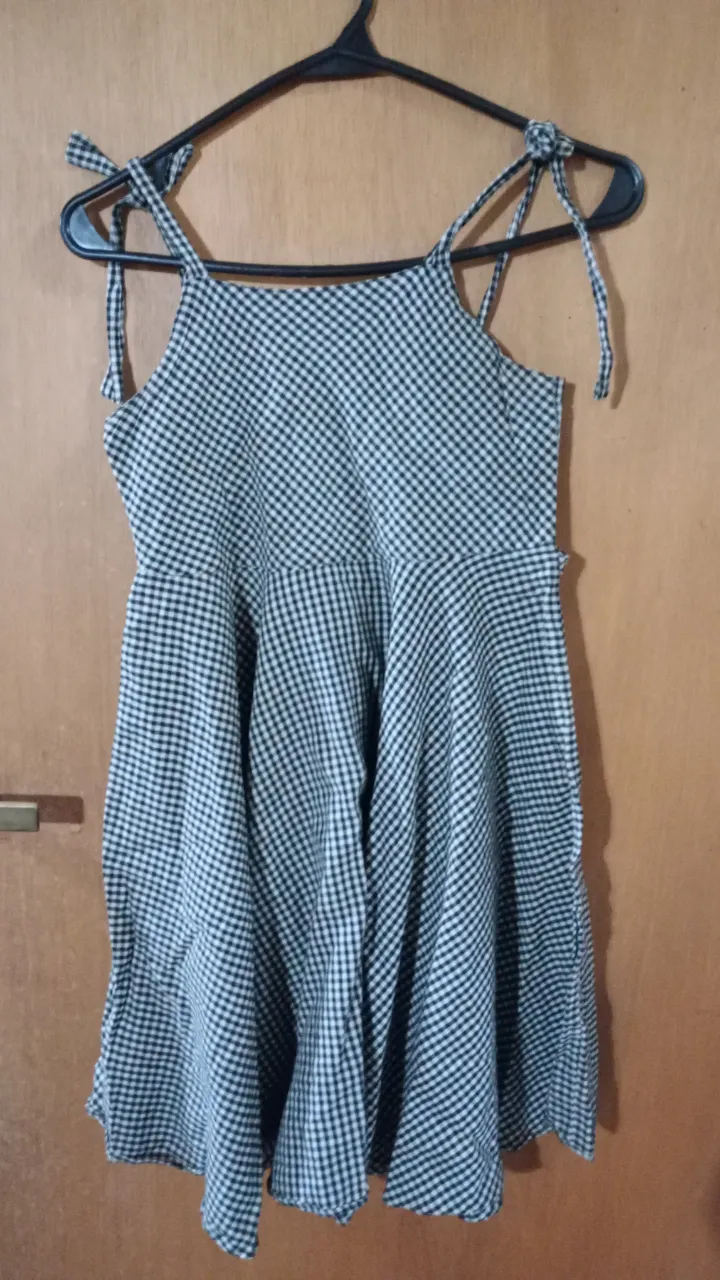 Vestido Grisino 8 años con estampado a cuadros blanco y negro. Tiene tirantes finos que se atan en los hombros y un corte en la cintura que le da vuelo a la falda. Ideal para un look casual y fresco.