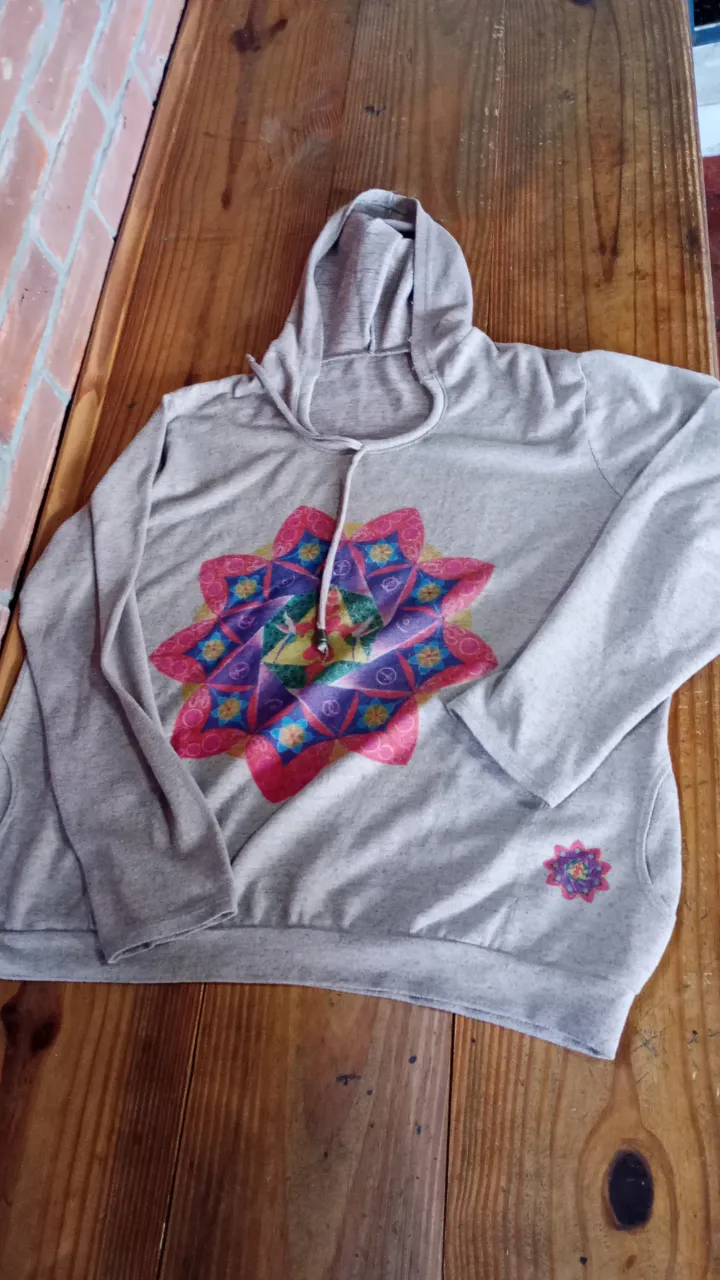Buzo canguro de mujer, de color gris con capucha y cordones. Estampado floral en el frente y un pequeño estampado en la manga. Ideal para un look casual y cómodo.
