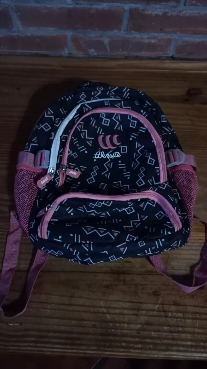 Mochila negra con detalles en rosa, ideal para uso diario o escolar. Cuenta con un diseño moderno y práctico, con múltiples compartimentos y correas ajustables.